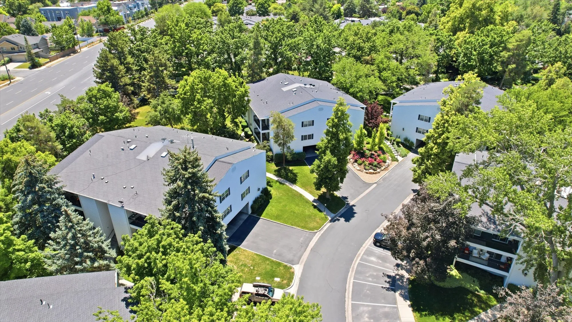 Multi-story buildings with white siding and dark roofs, surrounded by mature trees and manicured landscaping