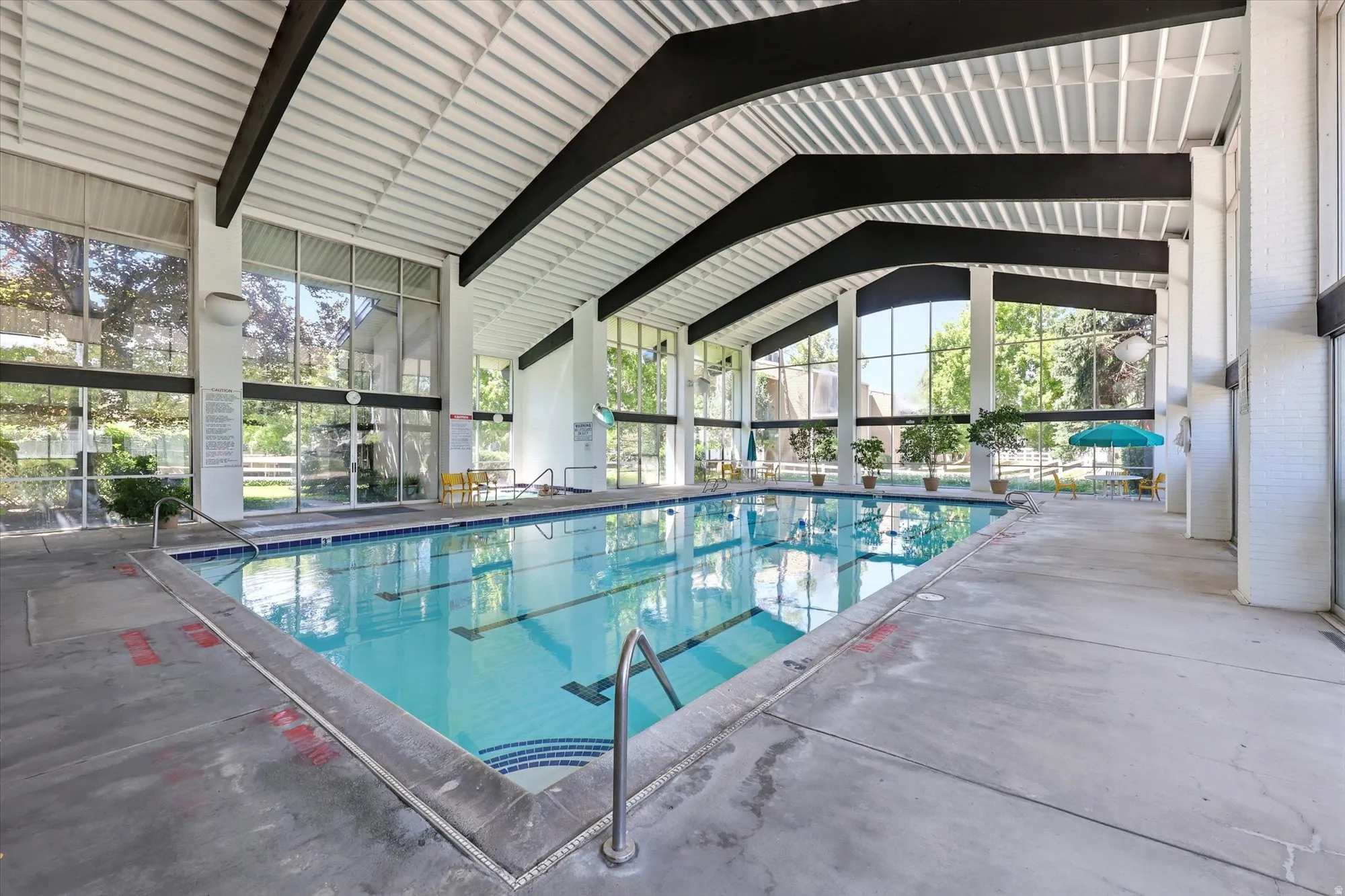 Indoor swimming pool featuring a lap lane, concrete decking, and vaulted ceilings with exposed beams