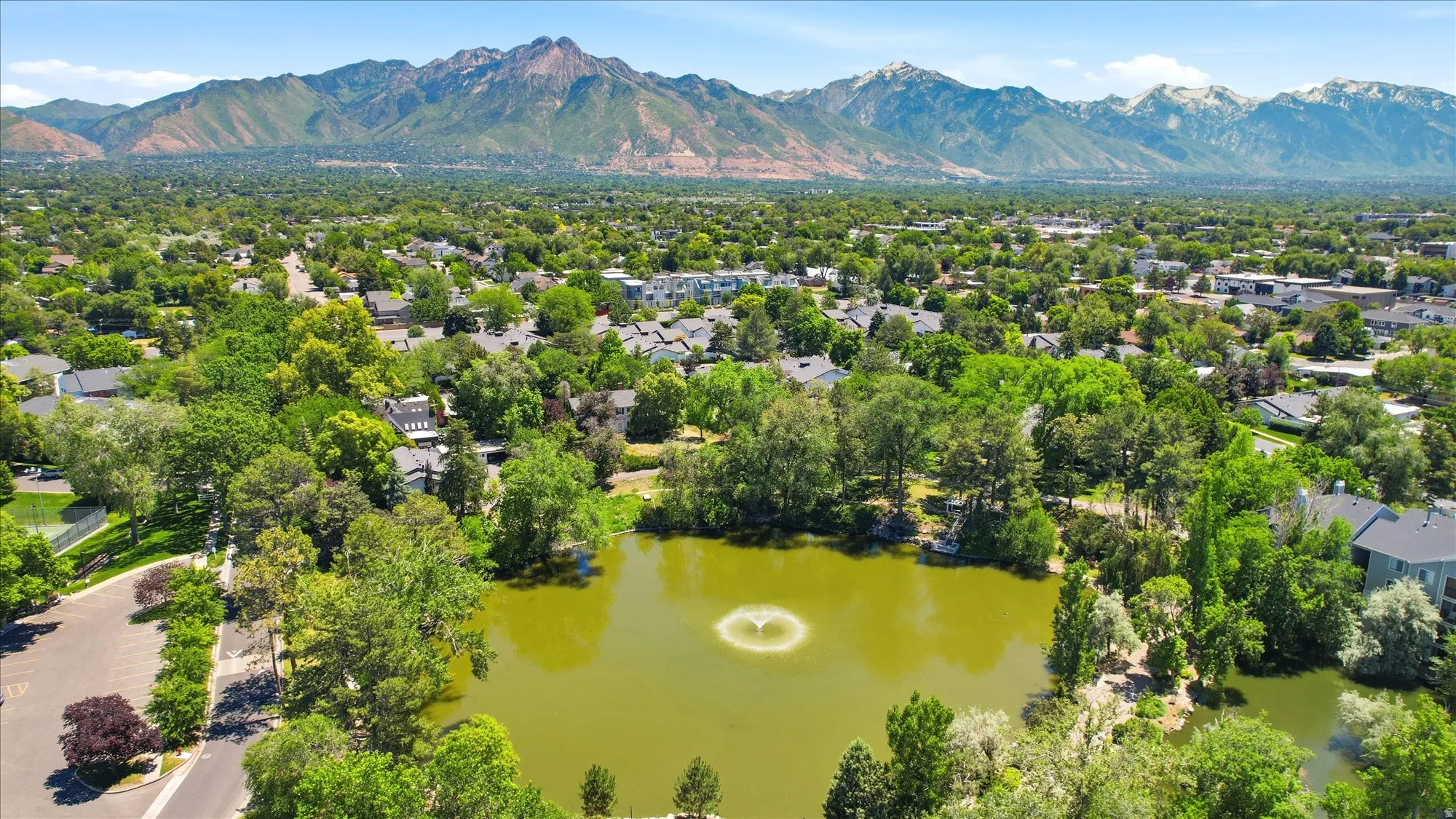 Aerial perspective featuring a community pond with a central fountain, surrounded by mature trees and residential structures