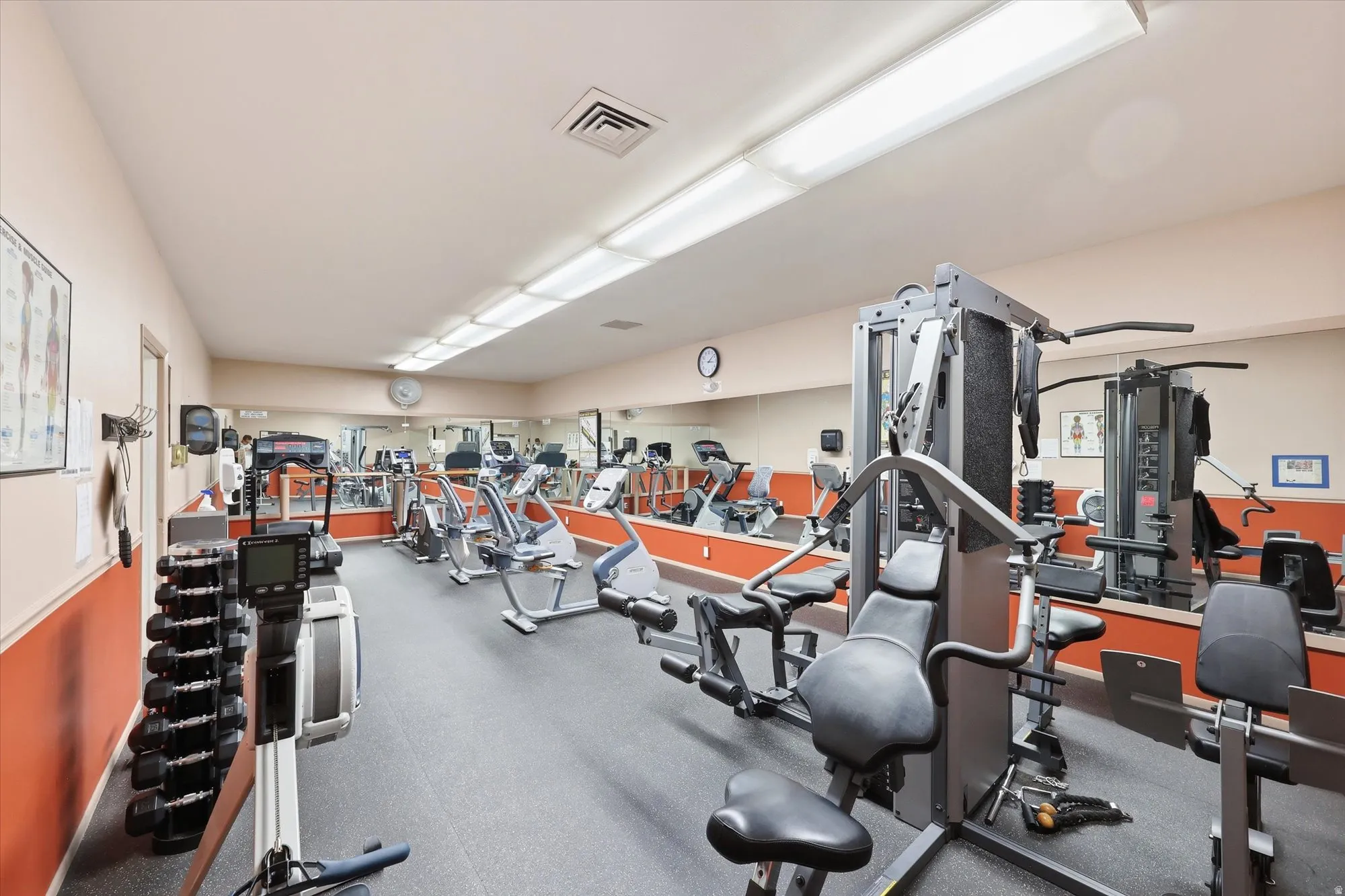 Fitness room featuring multiple exercise machines, mirrored walls, rubber flooring, and bright overhead lighting