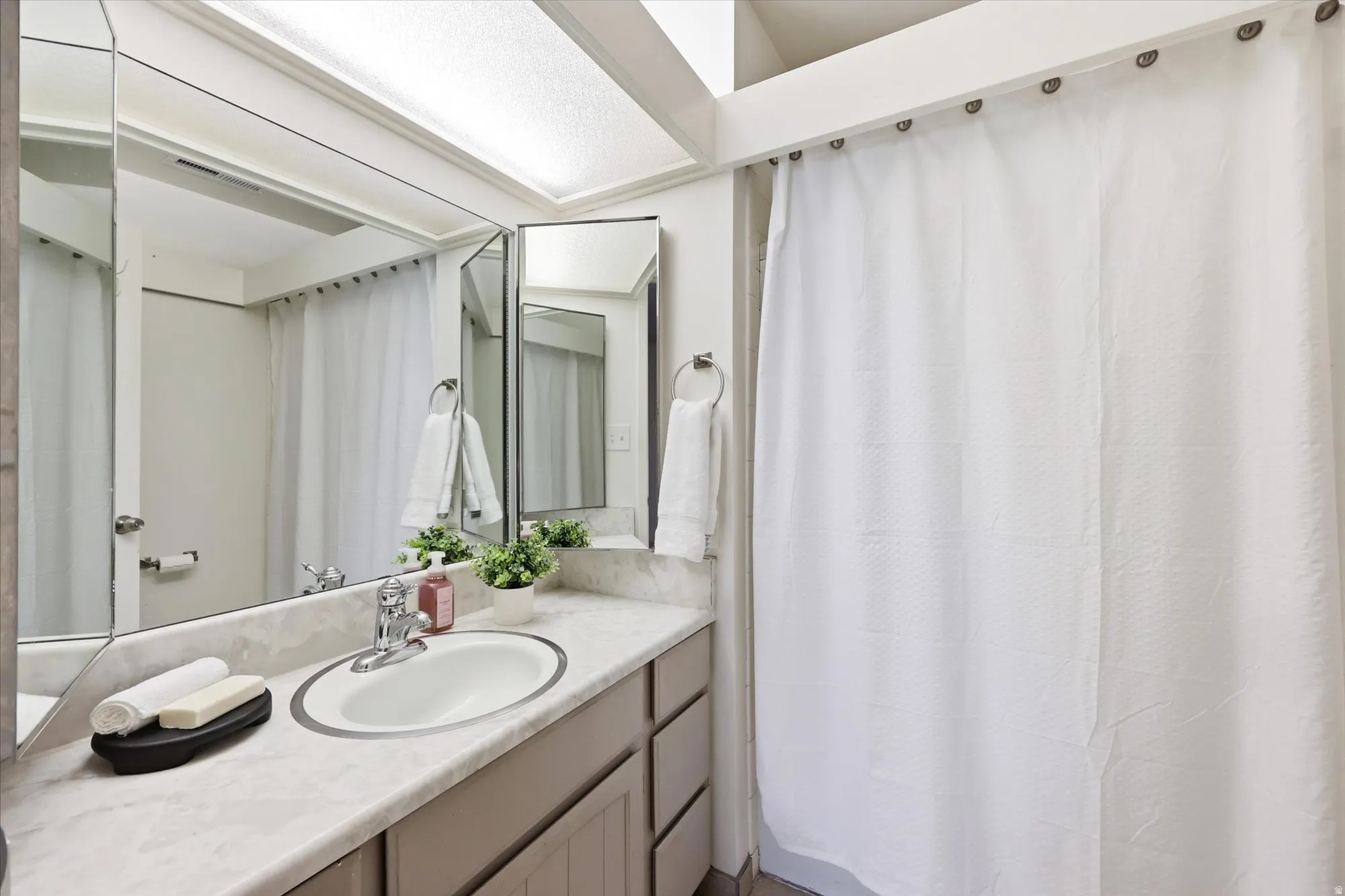 Bathroom featuring an elongated vanity with an integrated sink, a large wall-mounted mirror, and overhead lighting
