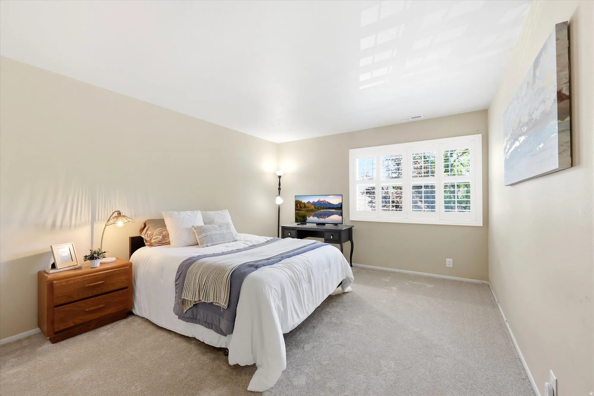 Bedroom featuring light-colored walls, grey carpet, and a large window with white plantation shutters