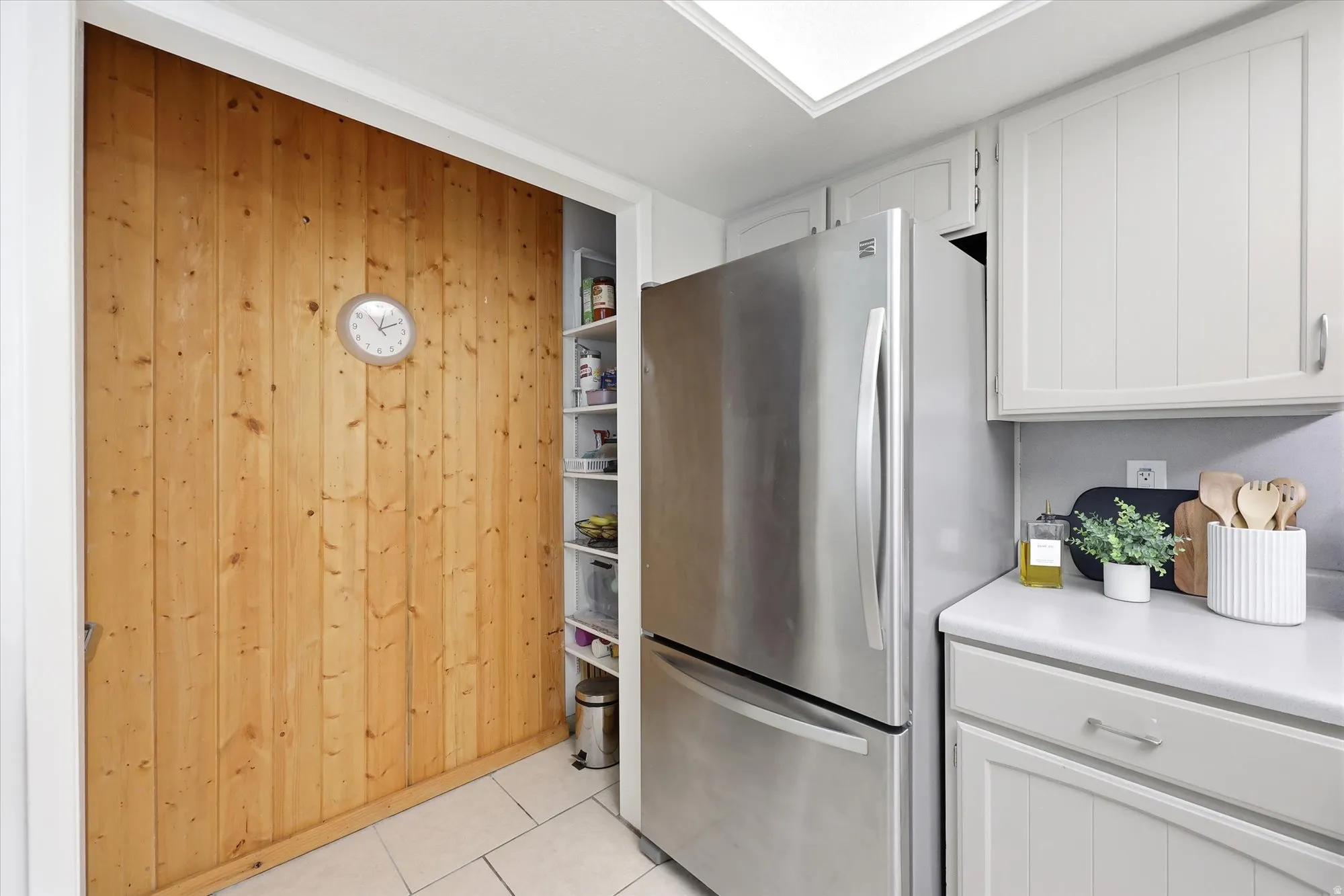 Kitchen featuring a stainless steel refrigerator, light-toned cabinetry, white countertops, tile flooring, and a large wood-paneled wall with a built-in storage area