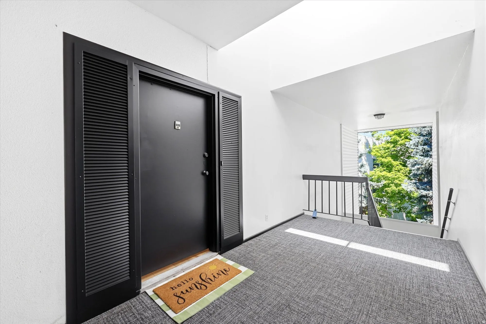 Entryway featuring a black door with louvered side panels, light-toned walls, and grey patterned carpet flooring