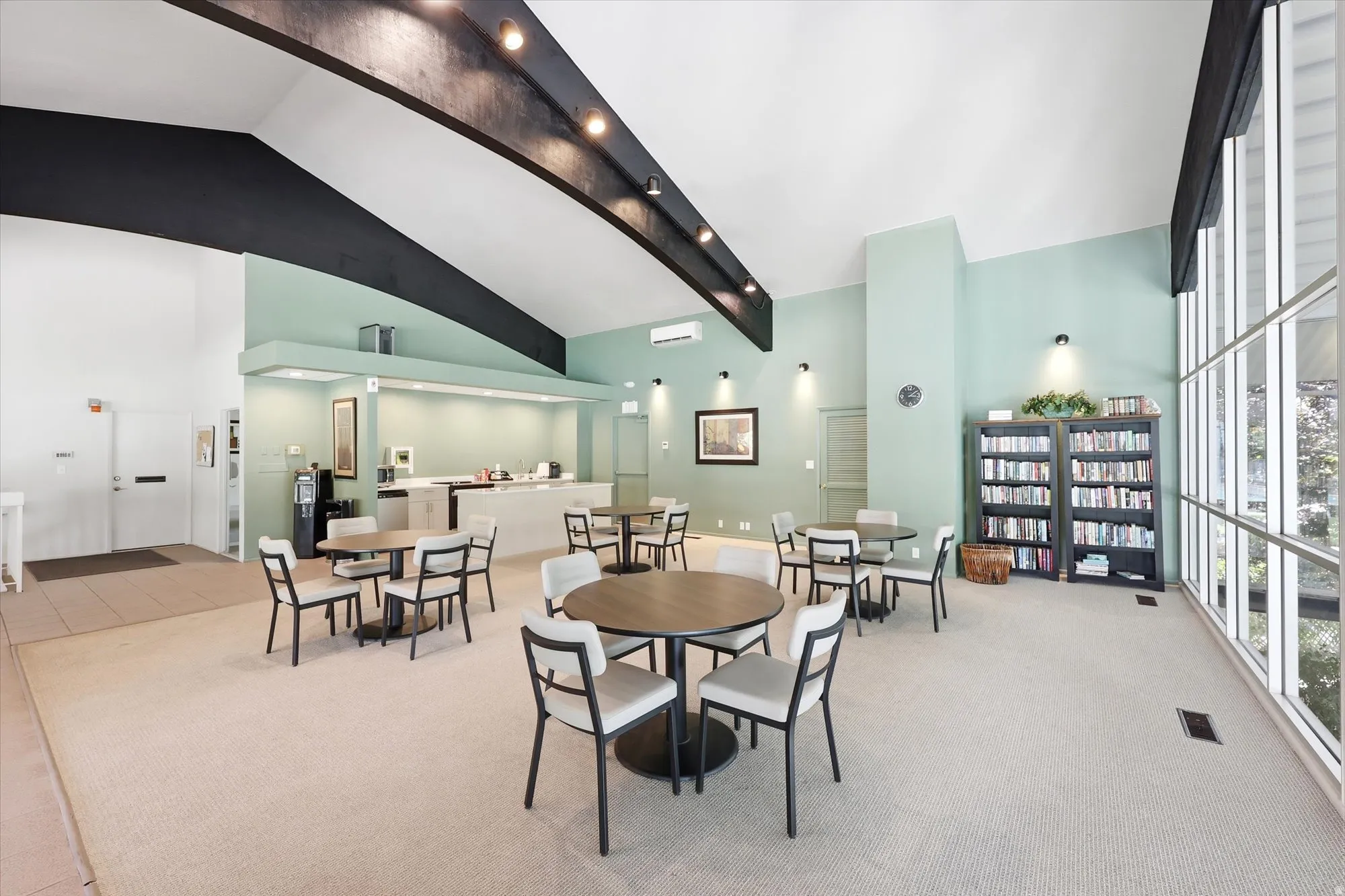 Spacious communal room featuring vaulted ceilings, floor-to-ceiling windows, and integrated track lighting