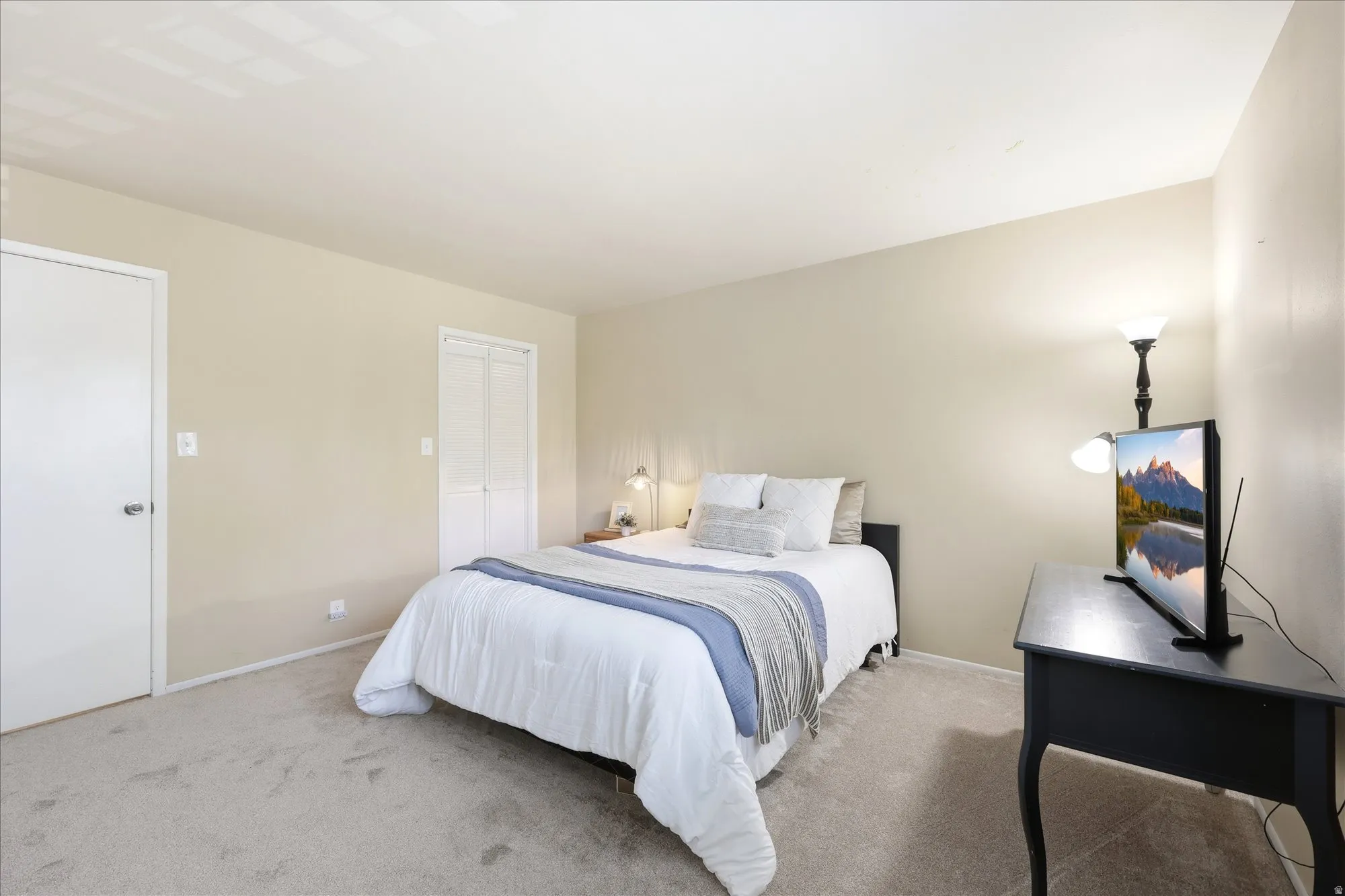 Carpeted bedroom featuring light-toned walls, a standard white door with a round knob, and bi-fold closet doors