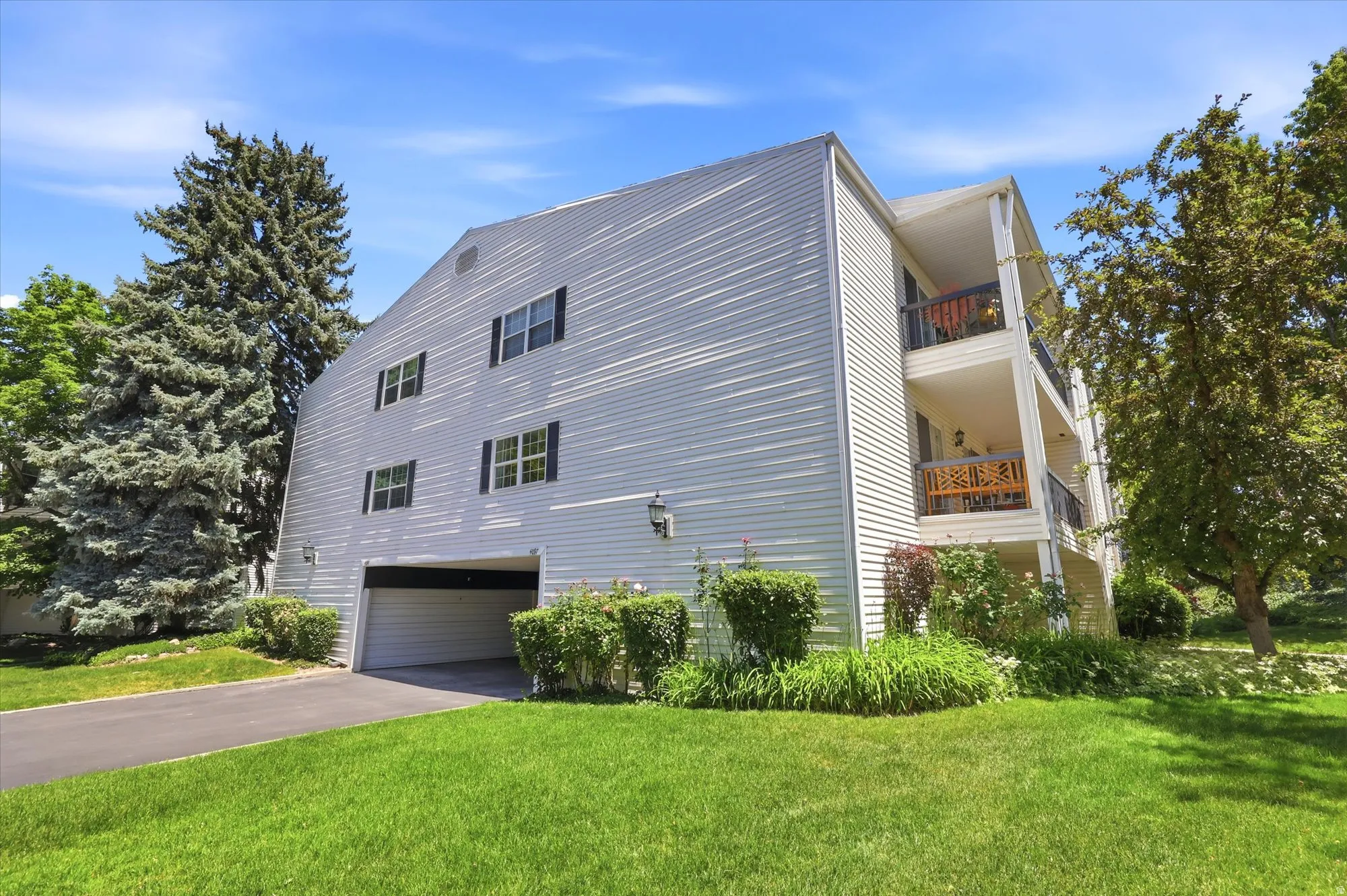 Multi-story building featuring white horizontal siding, multiple balconies with dark railings, a ground-level garage, and integrated wall sconces