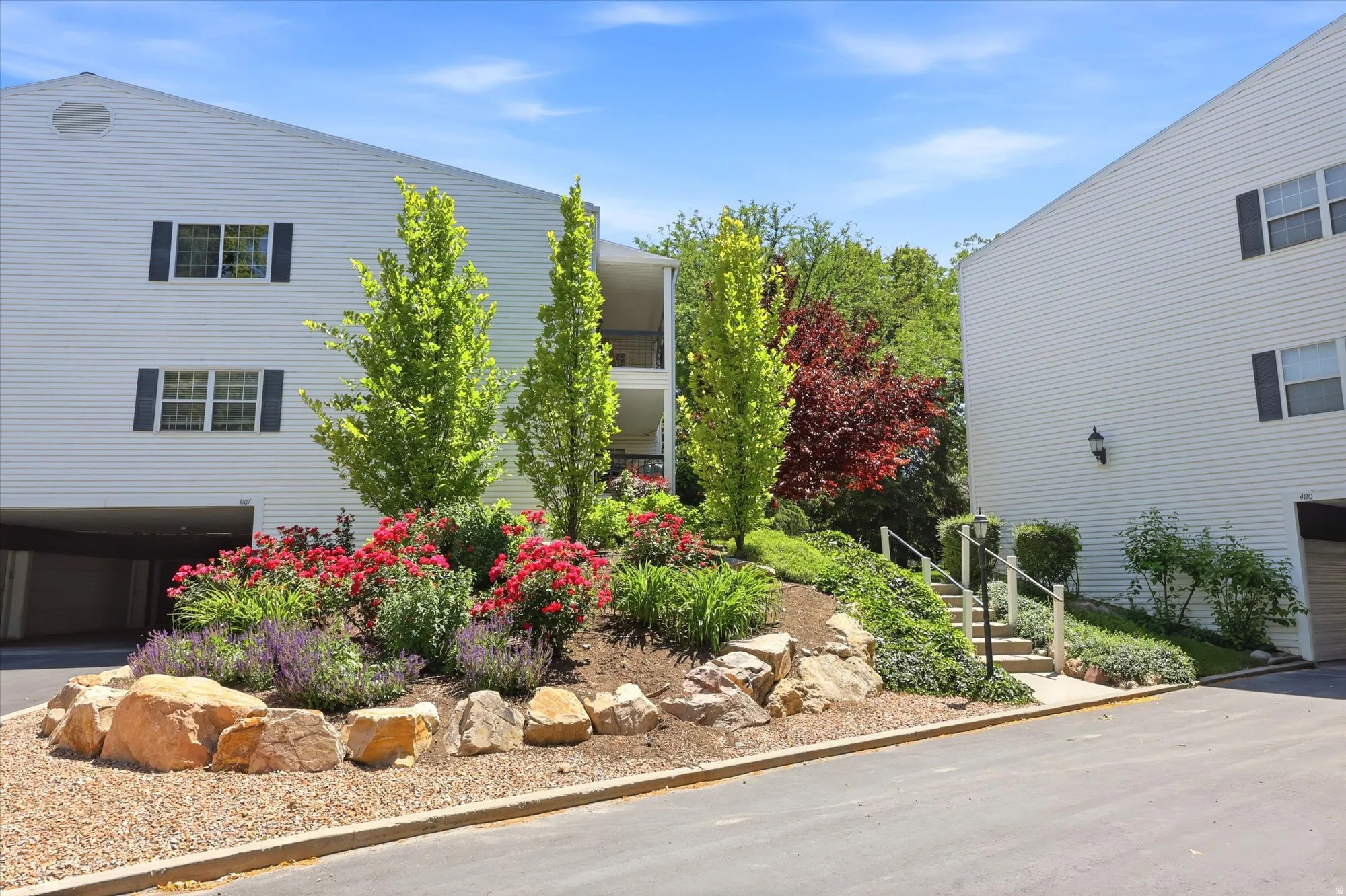 Landscaped entrance featuring a tiered rock garden with vibrant plantings and mature trees