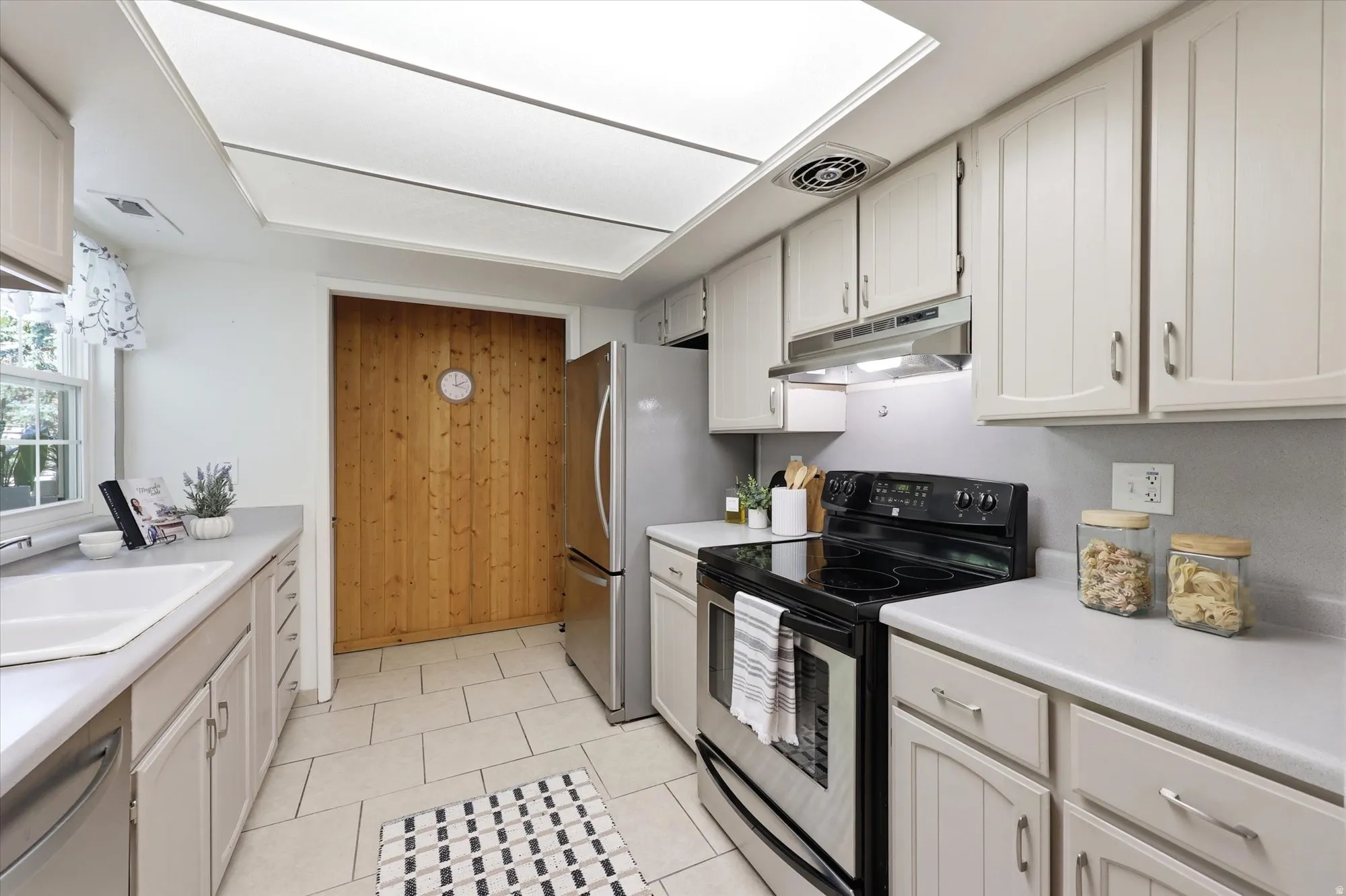 Kitchen featuring light-toned cabinetry, a stainless steel refrigerator, and a black and stainless steel range with overhead ventilation