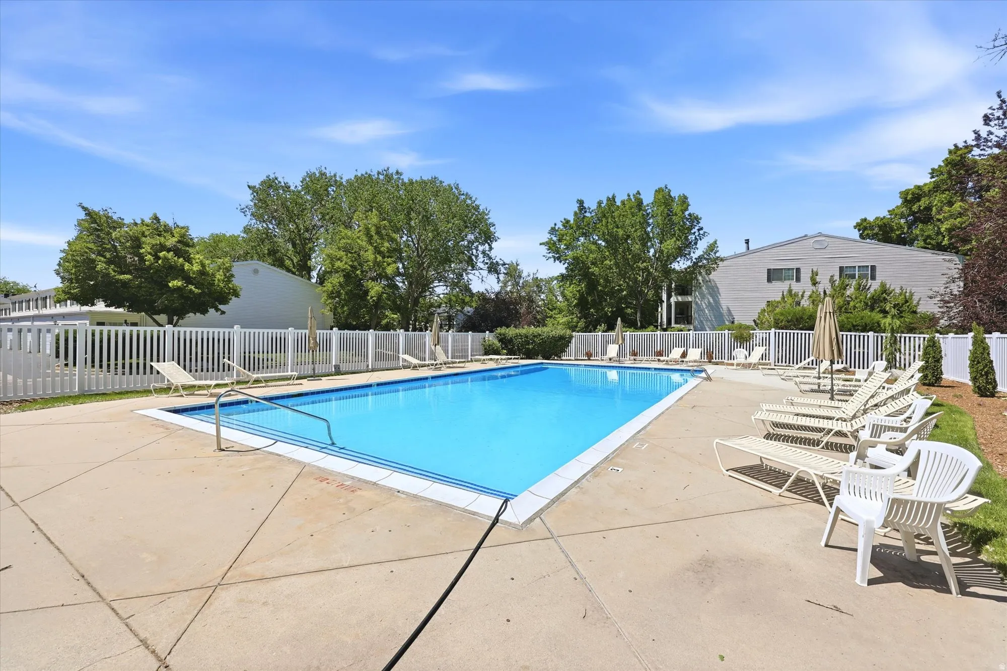 Outdoor swimming pool with concrete surround, white picket fencing, and mature perimeter trees