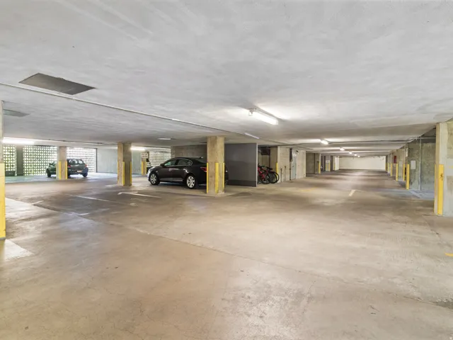 Subterranean parking garage featuring concrete flooring, concrete support columns with yellow protective wraps, and fluorescent overhead lighting