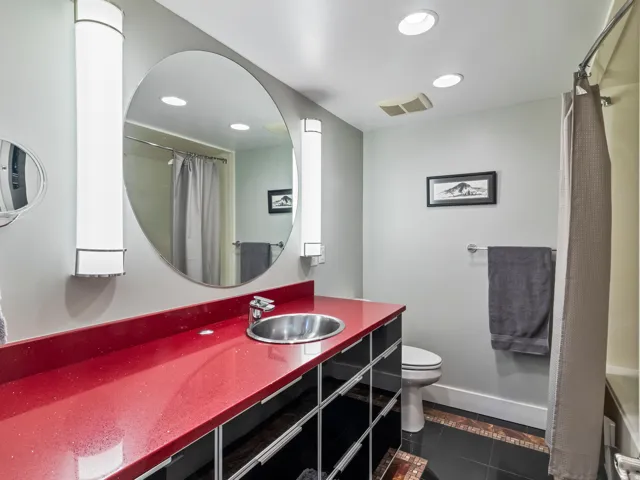 Bathroom featuring a circular mirror, red countertop, undermount sink, built-in cabinetry, and tile flooring