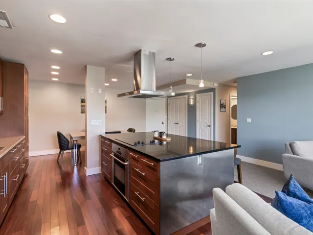 Contemporary kitchen island featuring an integrated cooktop, stainless steel oven, and overhead range hood