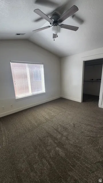 Spacious room featuring vaulted ceilings, a ceiling fan with integrated lighting, window blinds for light control, plush brown carpeting, and a closet with shelving