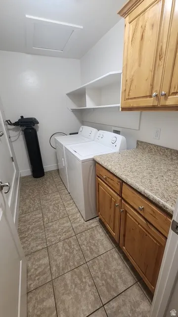 Utility room featuring wood cabinetry, stone-look countertop, integrated shelving, and tiled flooring