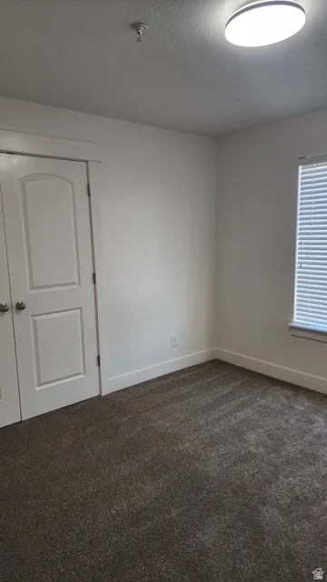Room featuring neutral wall tones, dark textured carpet, white trim, and a window with horizontal blinds