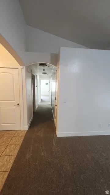 Long hallway with carpet flooring and an arched entryway