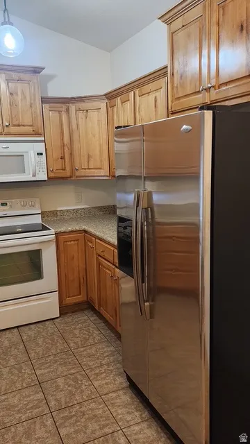 Kitchen featuring light wood cabinetry, stone-finish countertops, stainless steel refrigerator, white microwave, and tiled flooring