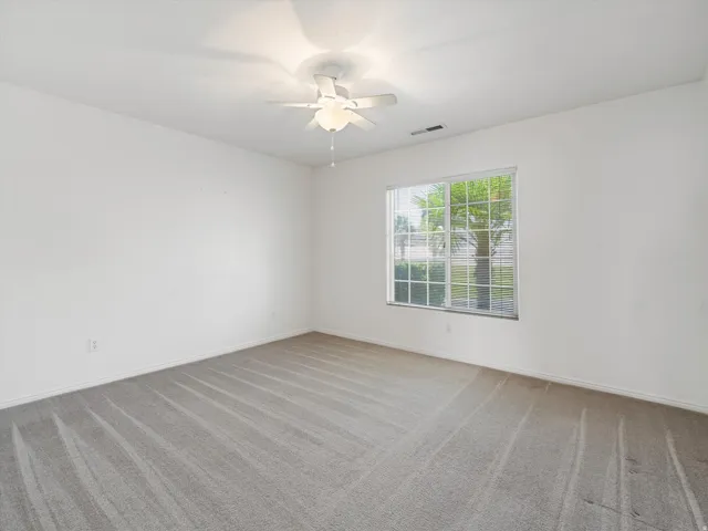 Bright room featuring a large window with horizontal blinds, overhead ceiling fan with lighting, carpet flooring, and white baseboards