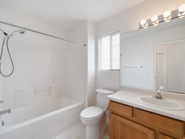 Bathroom featuring a white tub/shower combination with tiled surround, a toilet, and a vanity with a wood-finish cabinet and integrated sink