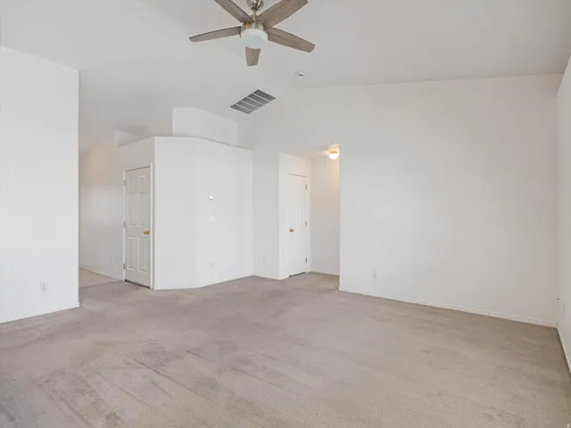 Spacious room featuring vaulted ceilings, light-colored carpeting, a ceiling fan with integrated lighting, and multiple interior doors