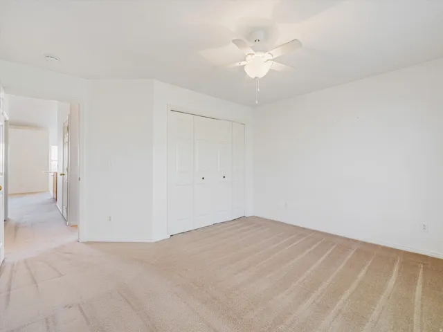 Carpeted room featuring a ceiling fan with integrated lighting, white walls, and bi-fold closet doors