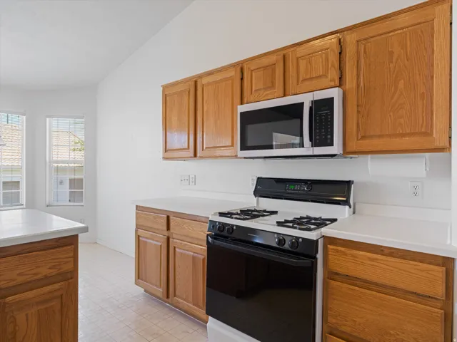 Kitchen featuring wood cabinetry, white countertops, a built-in microwave, a black and white range, and tiled flooring