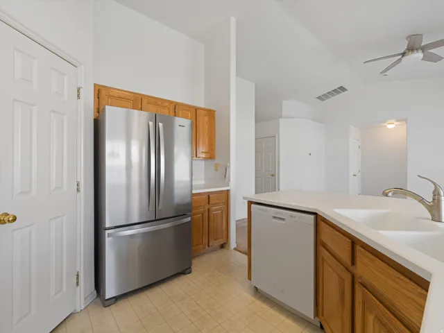 Kitchen featuring wood cabinetry, stainless steel refrigerator, white dishwasher, and a double basin sink with a gooseneck faucet