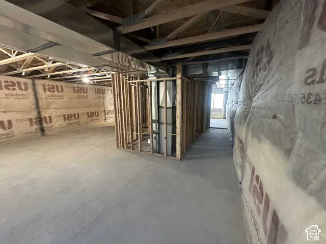 Unfinished basement space featuring exposed wooden ceiling joists, concrete flooring, and insulated walls