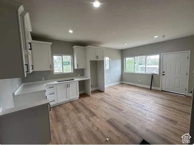 Open-concept living space featuring wood-finish flooring, recessed lighting, and a white kitchen with stone countertops and matte black hardware