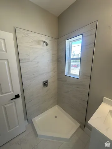 Corner shower with light-toned tiled walls, a window inset, and a chrome shower head and controls