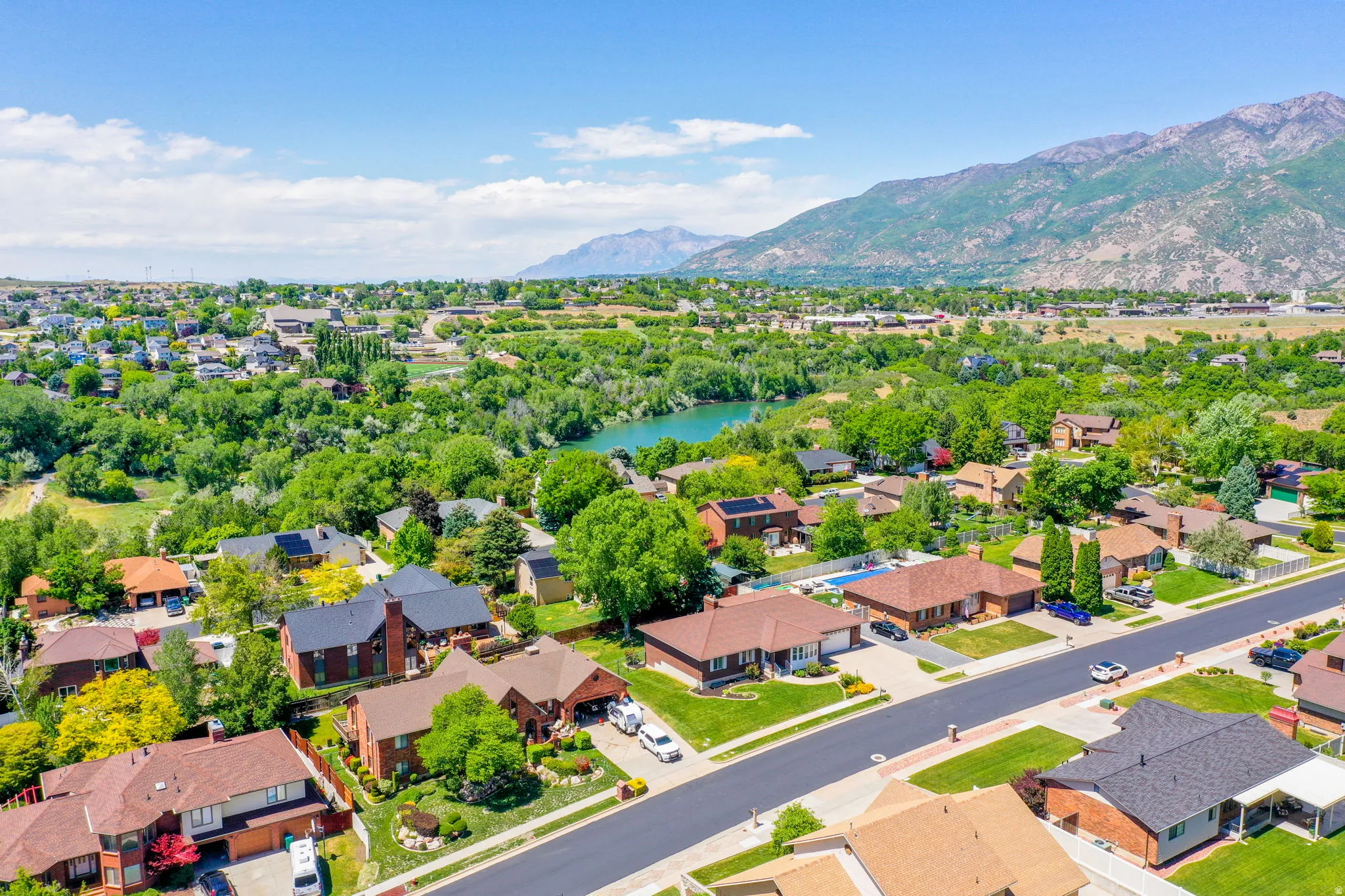 Aerial perspective showcasing a residential area with mature trees, green landscaping, a prominent body of water, and distant mountains