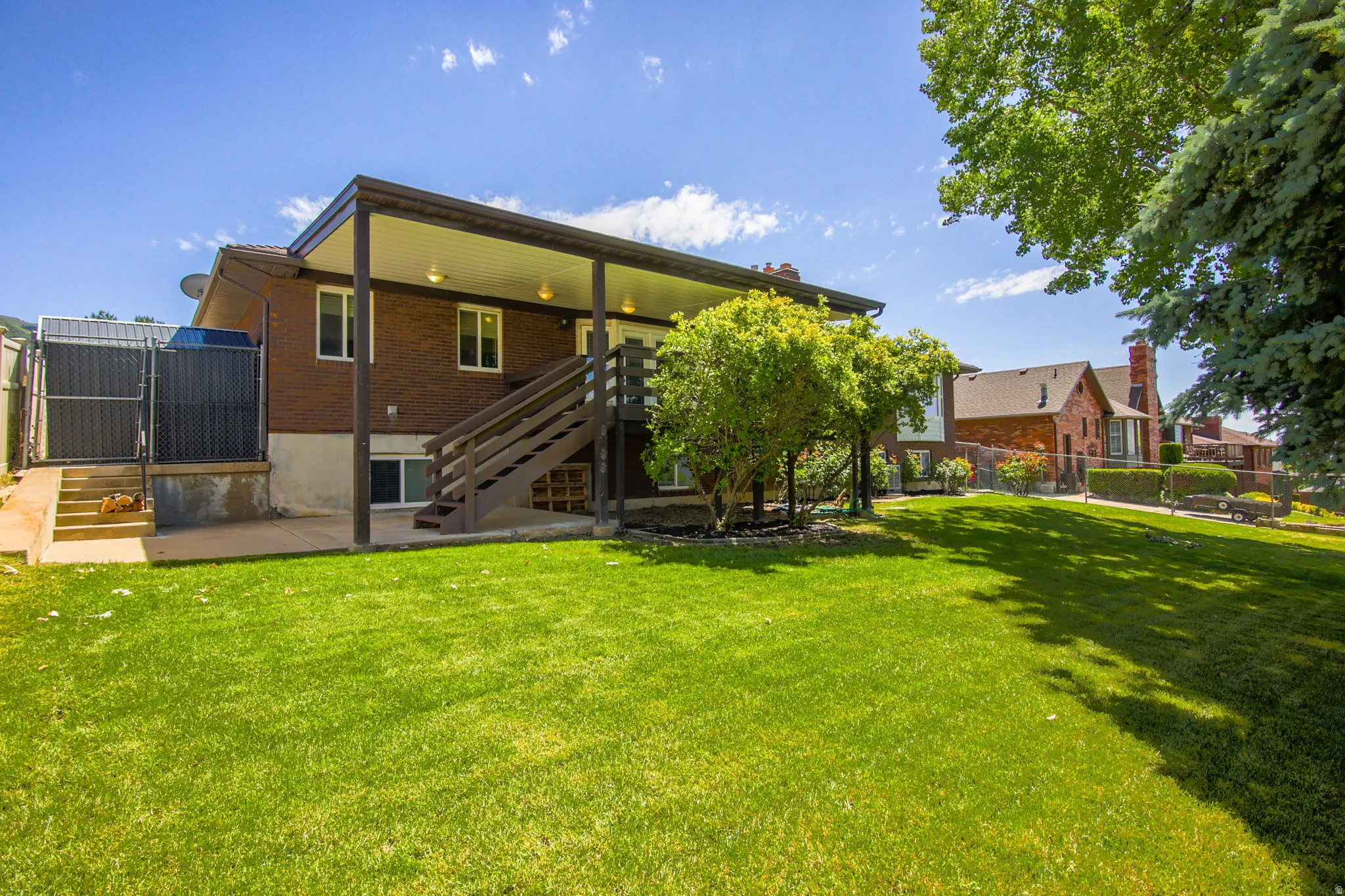 Expansive green lawn with a brick exterior home featuring a covered patio and a wooden staircase
