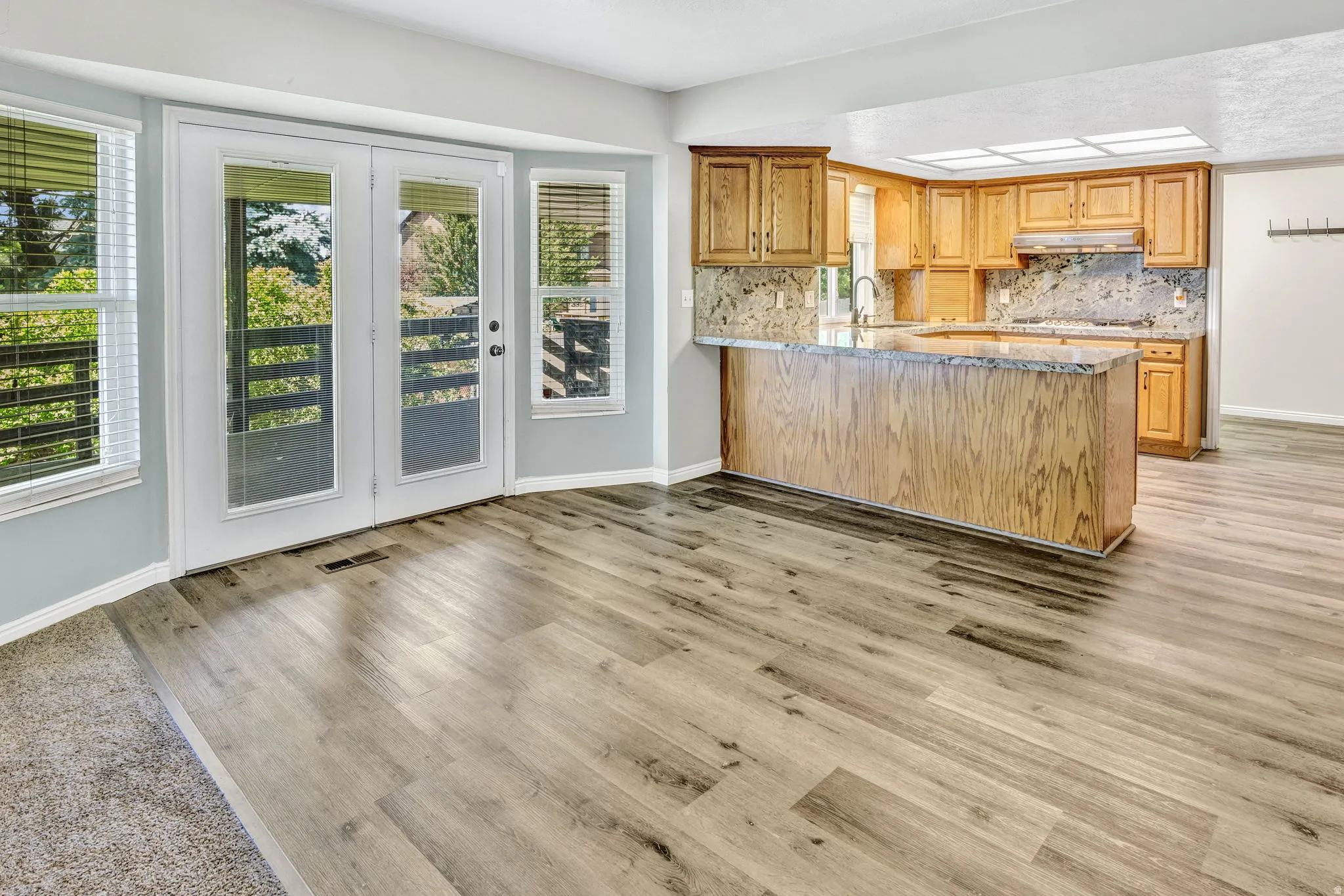 Spacious interior featuring wood-finish flooring, light blue wall paint, and a kitchen with warm-toned cabinetry, a stone-finish countertop, and a matching backsplash