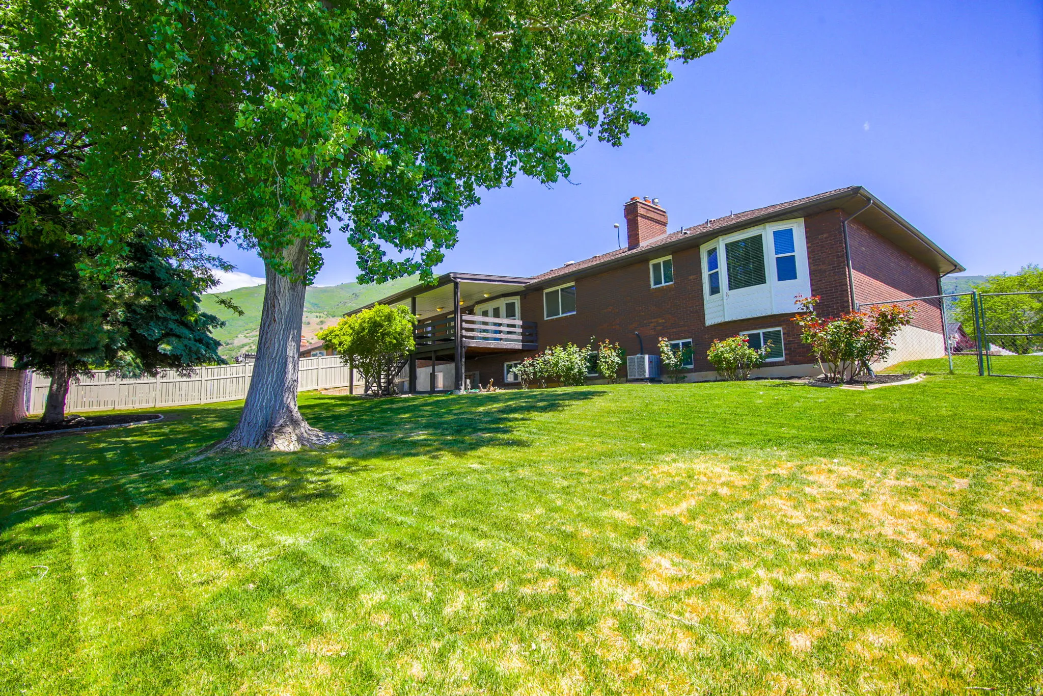 Expansive backyard featuring a manicured lawn, established shade trees, and a two-story brick exterior