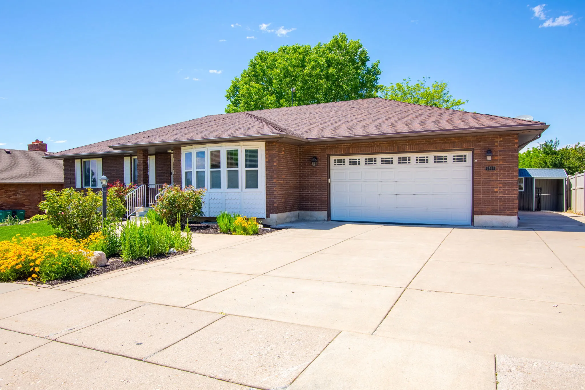 Brick exterior with a brown shingle roof, featuring a two-car garage with a white door, bay window, and concrete driveway