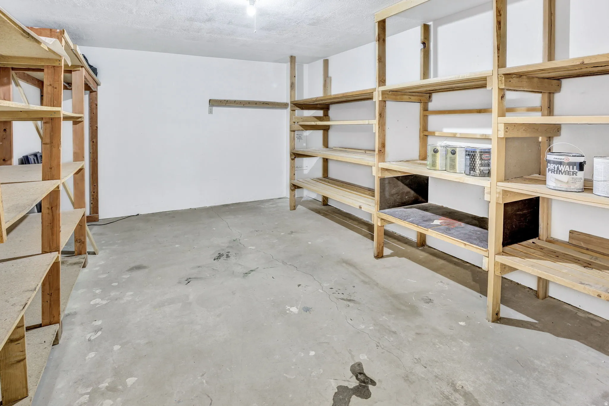 Spacious storage area featuring concrete flooring, white walls, and extensive built-in wooden shelving for organization