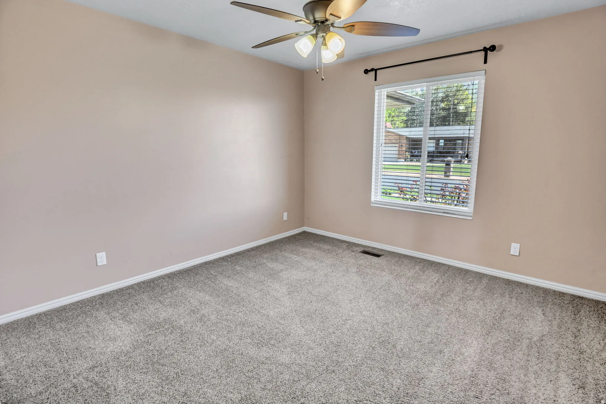 Bright room featuring a large window with blinds, a ceiling fan with integrated lighting, neutral-toned walls, and grey carpeting