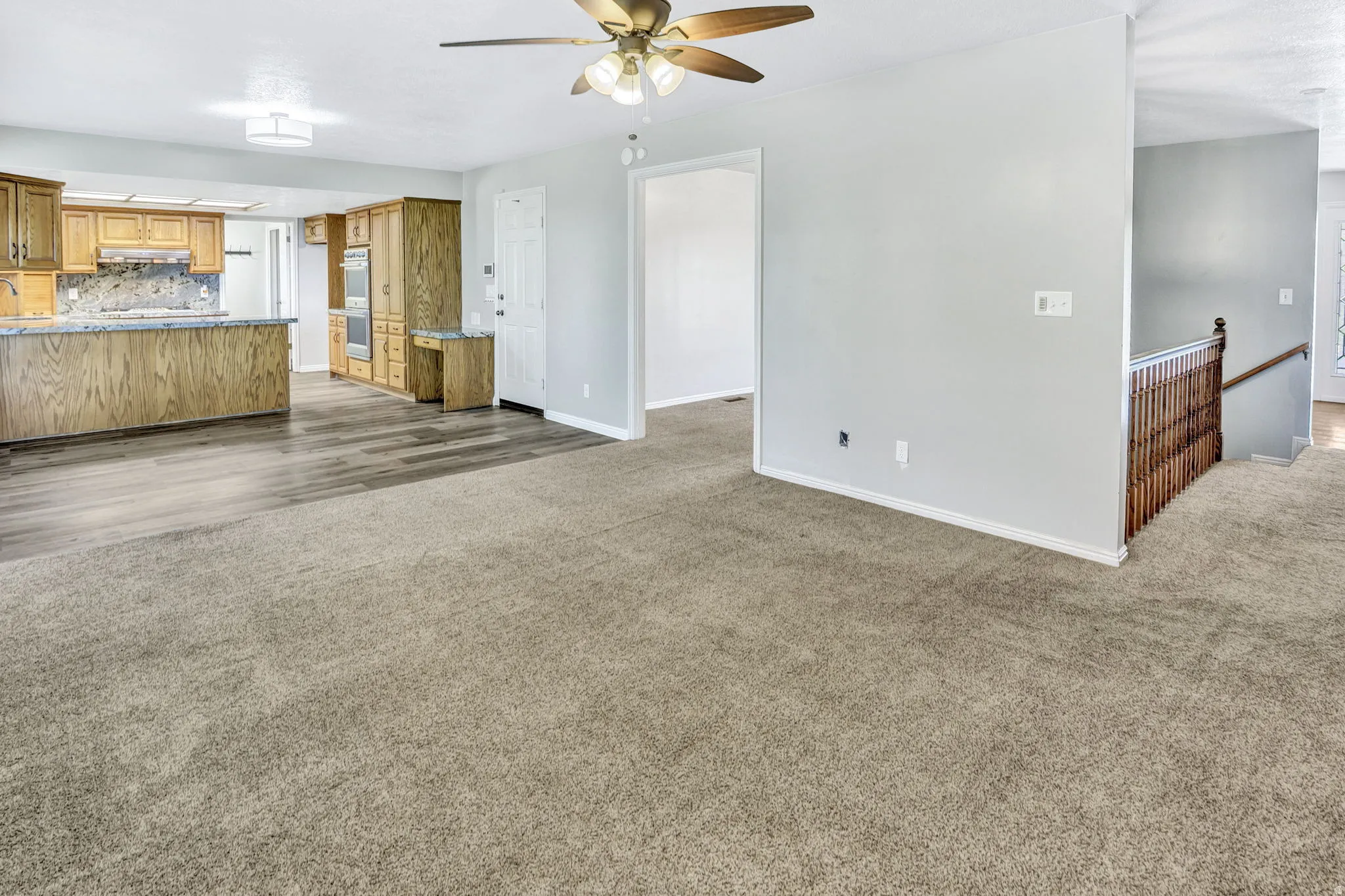 Open-concept living area featuring a ceiling fan, light gray wall finishes, and carpet flooring