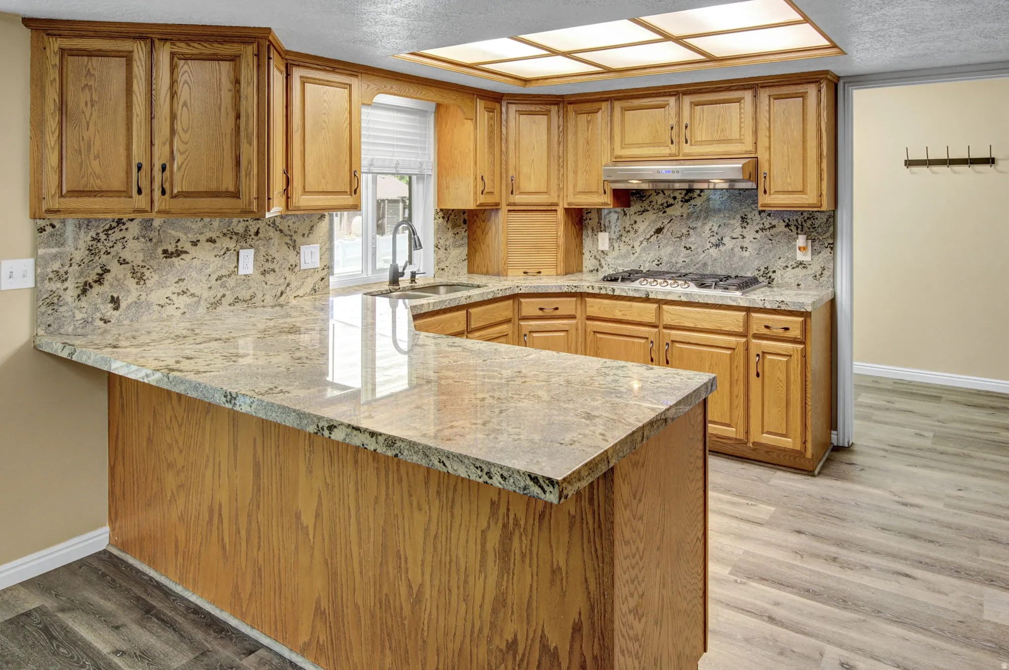 Kitchen featuring light wood cabinetry, stone countertops, integrated gas range with overhead ventilation, and a built-in sink