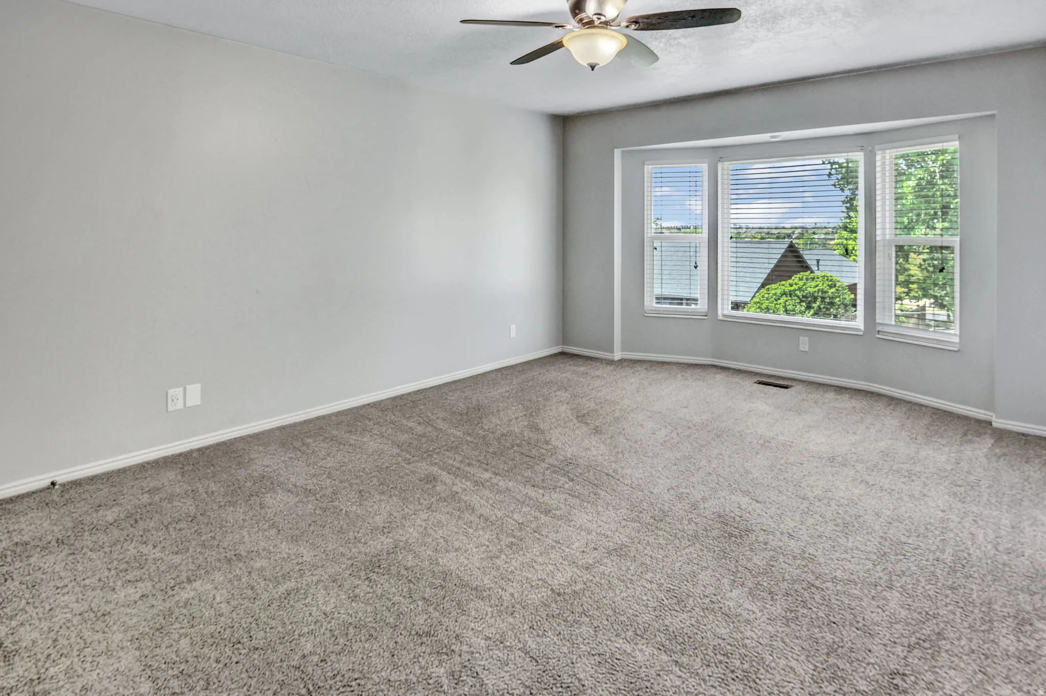 Carpeted room featuring a bay window with blinds, a ceiling fan with integrated lighting, and light gray painted walls