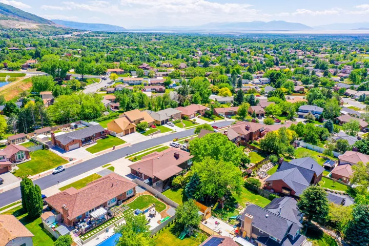 Expansive residential neighborhood featuring a variety of architectural styles, mature trees, mountain backdrop, and distant water body