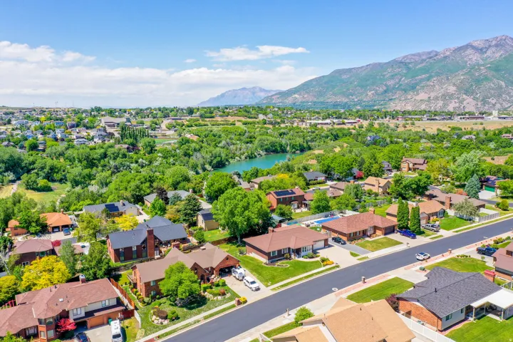 Aerial perspective showcasing a residential area with mature trees, green landscaping, a prominent body of water, and distant mountains