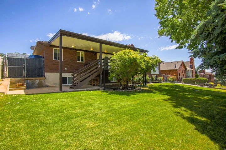 Expansive green lawn with a brick exterior home featuring a covered patio and a wooden staircase