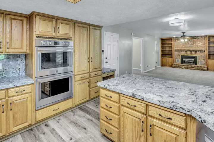 Kitchen featuring light wood cabinetry, stone countertops, and stainless steel double ovens