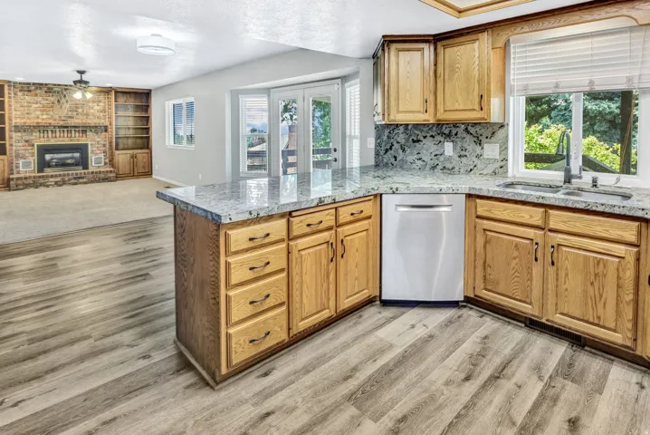 Kitchen featuring stone countertops, natural wood cabinetry, stainless steel dishwasher, and wood-finish flooring