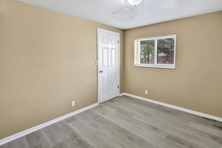 Spacious room featuring wood-finish flooring, neutral-toned walls, a paneled door, and a multi-pane window with blinds