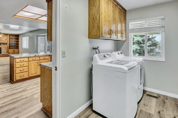 Dedicated laundry area featuring overhead cabinetry, light wood-finish flooring, and a window with white blinds