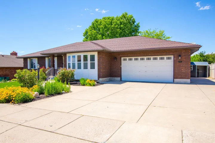 Brick exterior with a brown shingle roof, featuring a two-car garage with a white door, bay window, and concrete driveway