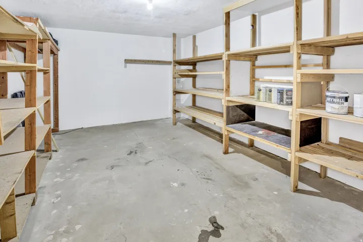 Spacious storage area featuring concrete flooring, white walls, and extensive built-in wooden shelving for organization